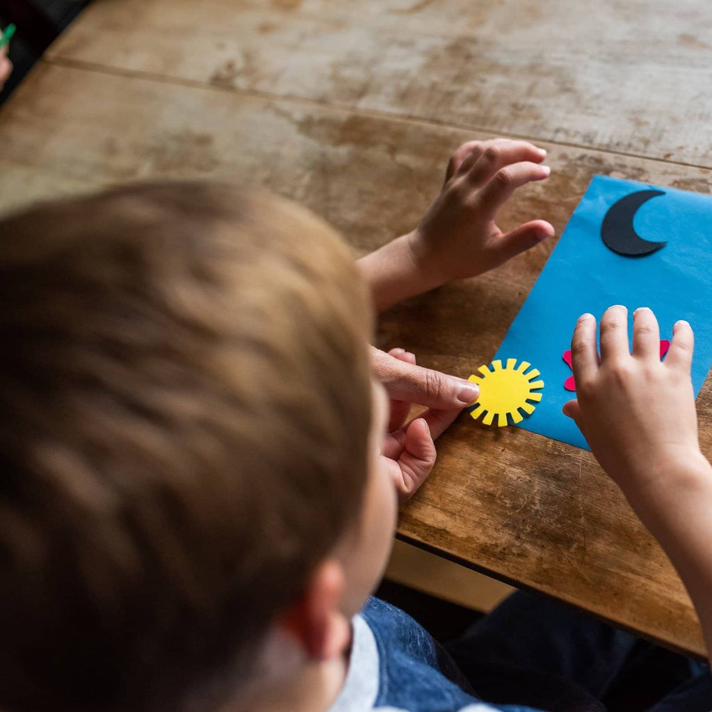 Child working on a craft. They are placing stencils on sun paper to create a design.