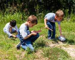 Three kids on a scavenger hunt. They are looking for items on the card and collecting fun nature souvenirs..